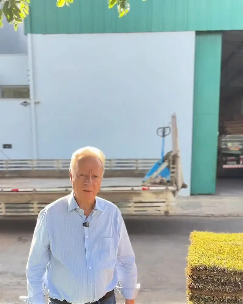 Seu Cesa, fundador da Grameira Sinop, em frente ao galpão ao lado de paletes de grama
